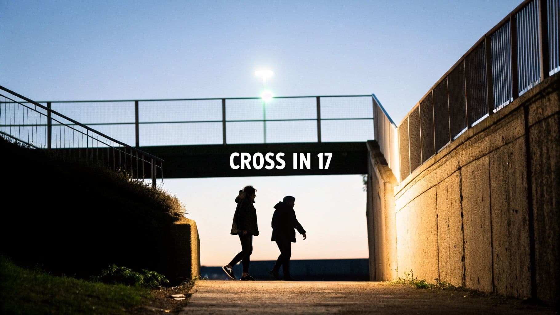 Two silhouetted figures walk under an urban underpass with concrete walls and railings at dusk.